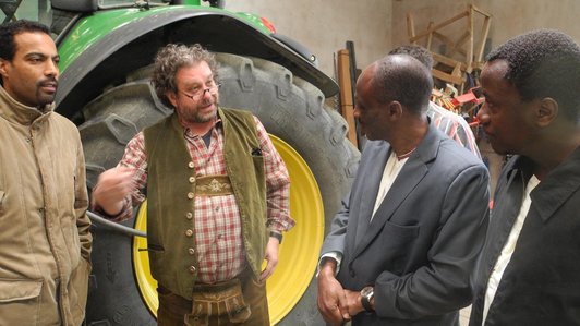 A group of man standing in front of a tractor looking and talking to each other