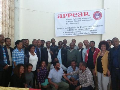 Group of people posing for a picture under a big APPEAR poster