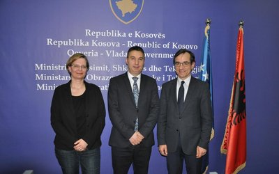 Herr Shyqiri Bytyqi (MEST), Frau Veronika Nitsche (WUS Austria) und Ulrich Hörmann posieren vor blauem Hintergrund mit Kosovo Wappen