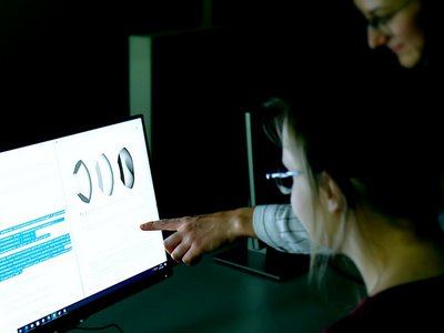 Zwei Schülerinnen sitzen vor einem Computerbildschirm. Eine davon zeigt auf das Display. 