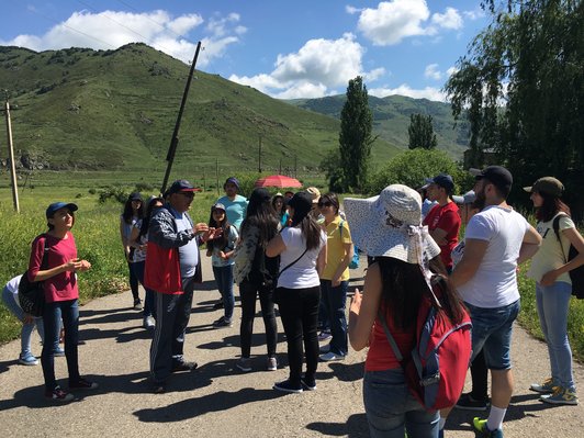 Man explains something to a group of people standing in green landscape