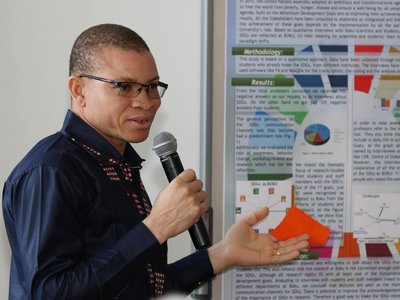 Vincent-Paul Sanon talking into a microphone with a poster next to h im