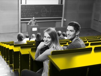 A student and a student are sitting in the lecture hall and laughing at the camera.