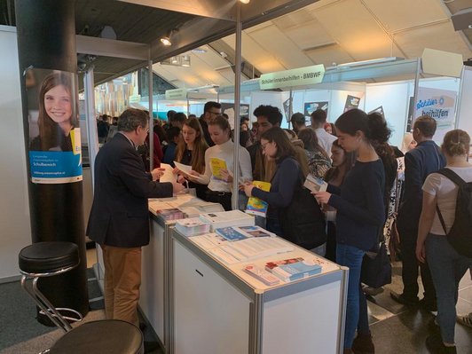 Ein Mitarbeiter des OeAD berät Schülerinnen und Schüler am Messestand.