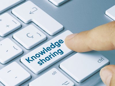  A finger presses the Enter key on a keyboard. The button is labeled with the words: Knowledge Sharing