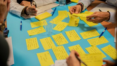 Mehrere Personen beschriften bunte Zettel, die auf einem Tisch liegen