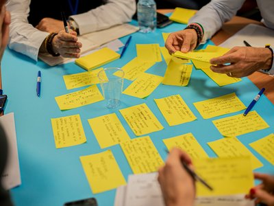 Mehrere Personen beschriften bunte Zettel, die auf einem Tisch liegen