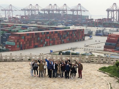 A port with ships, containers, cranes and a group of people looking at the camera.