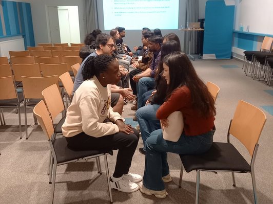 Photo of scholarship holders sitting in two rows, facing each other and engaging in a speedfriending activity