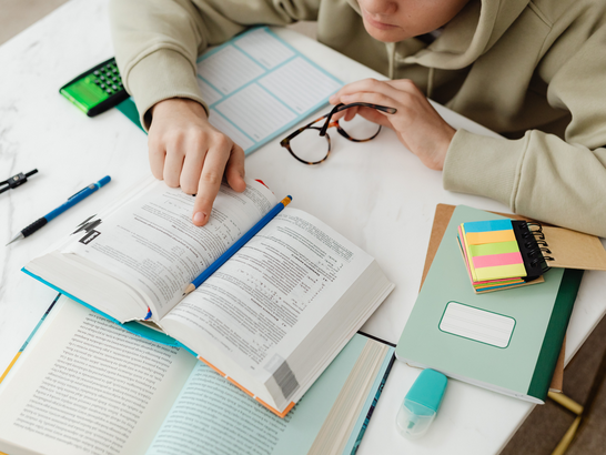 Ein Student liest ein Buch und hält eine Brille in der Hand.