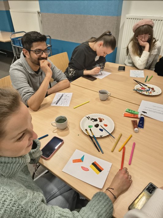 Photo of scholarship holders sitting around a table and painting pictures about their studies