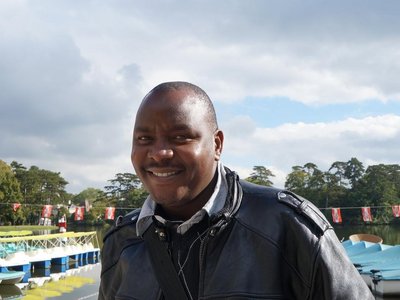 A man is standing in front of a lake and smiling into the camera.