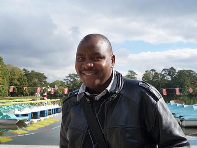 A man is standing in front of a lake and smiling into the camera.