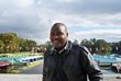 A man is standing in front of a lake and smiling into the camera.