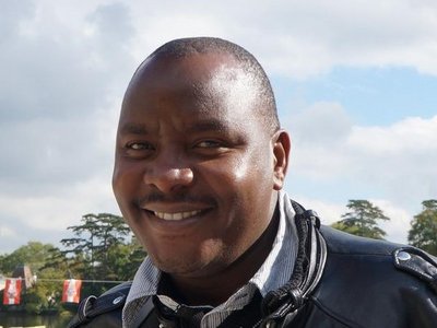 A man is standing in front of a lake and smiling into the camera.