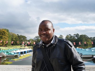 A man is standing in front of a lake and smiling into the camera.