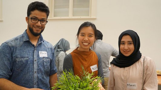 One man and two women standing behind a bar table with a green plant on it