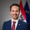 Ein Mann in Anzug blickt in die Kamera, hinter ihm die österreichische und EU-Flaggen