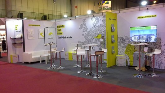 The Austrian trade fair stand at the EAIE Sevilla 2017 with tables and chairs in a yellow and black design.