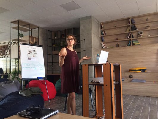 Woman standing behind a desk with notebook holding up her hands and look at something