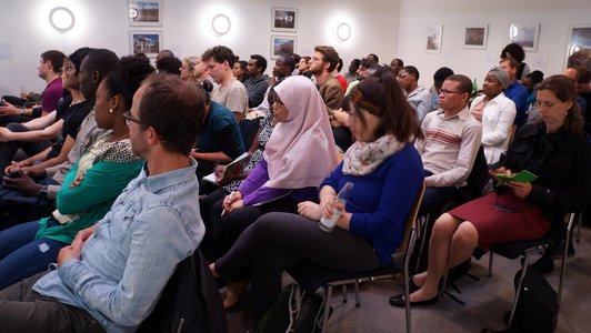 The picture shows an audience of approximately 40 people sitting on chairs and looking to the front.