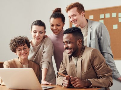 Glückliche Lehrpersonen stehen versammelt um einen Laptop