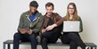 Three students, two men, one woman, holding a laptop.