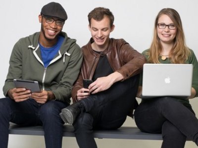 Drei Studierende, zwei Männer, eine Frau, die einen Laptop in der Hand hält.