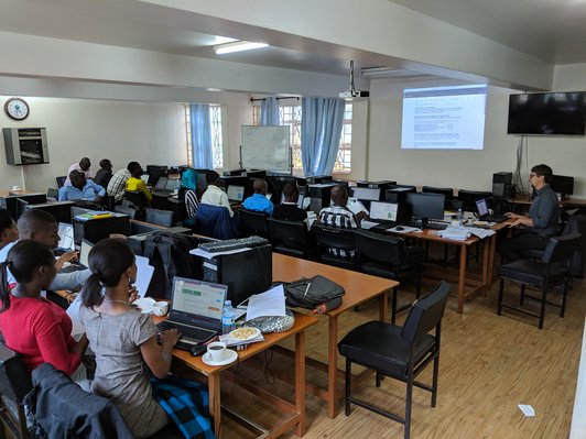 People sittin in rows on workplaces with notebooks looking at a presentation in front of them