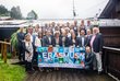 Ein Gruppenfoto, draußen vor einen Haus. Die Personen ganz vorne halten ein Erasmus+ Stoffplakat. Es herrscht Hochnebel.