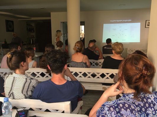 Group of people sitting in rows and looking at a presentation on a wall in front of them