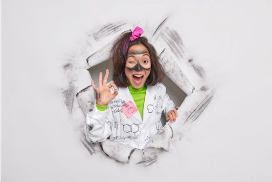 Ein Mädchen zeigt das Zeichen für ok und hat einen Laborkitel an