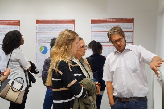 Man pointing at something on a poster of the poster presentation explaining something to two women