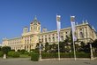 The Vienna Natural History Museum from the outside with two flags waving in the wind and a blue sky.