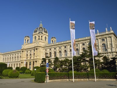 Das naturhistorische Museum Wien von Außen mit zwei wehenden Fahnen im Wind und blauem Himmel.