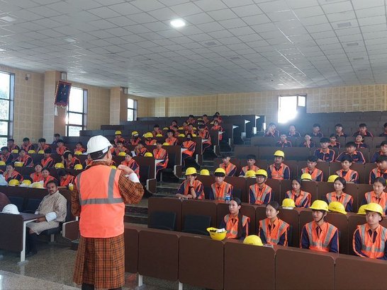 Bhutanese students in a lecture hall waring safety vests and helmets