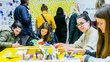 Young people doing crafts in class. They are sitting on a yellow table. In the background is a wall with favorite words.