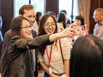 Zwei Alumni machen ein Selfie mit dem Geschäftsführer vom OeAD Jakob Calice. Im Hintergrund sind andere Personen in kleinen Gruppen verschwommen zu sehen.