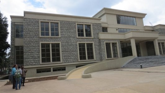 Three people standing in front of a building out of rocks with ramp and stairs as entrance