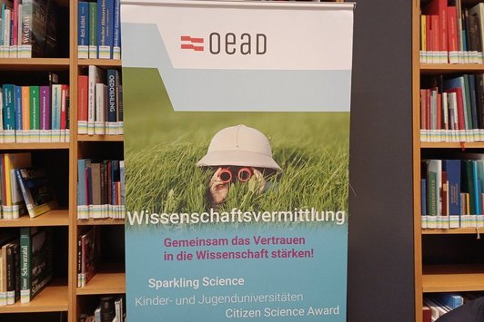 Das OeAD Public Science Roll up vor Bücherregal