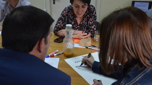 Group of people are sitting around a table and one woman is writting something on a poster