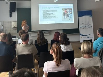 Vortragende mit Leinwand und Präsentation vor Zuschauer:innen