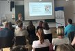 Vortragende mit Leinwand und Präsentation vor Zuschauer:innen