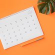 Kalender liegt auf orangener Unterlage, daneben sieht man ein Monstera Blatt