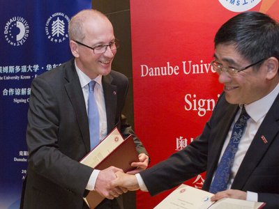 Rector of the Danube University Krems, Friedrich Faulhammer and Tong Shijun shake hands and each hold a document in their hand