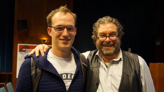 Andreas Melcher and another man are standing in an auditorium, smiling.