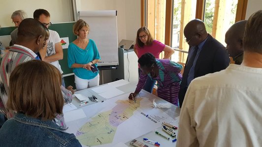 Group of people standing around a table and look at one woman drawing something on a poster