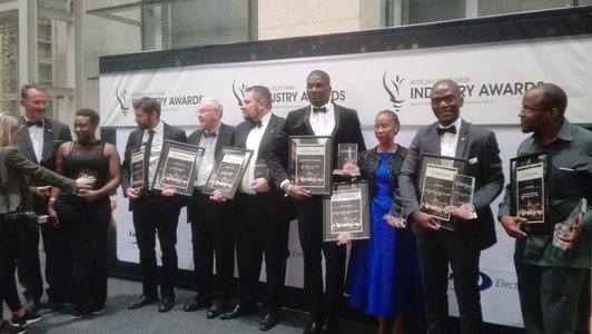 A group of eight people receiving awards, stand in front of a large roll-up announcing the African Utility Week Industry Awards