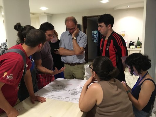 Group of people standing around a table and looking at a poster on it