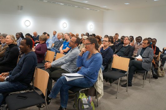 An audience of approximately 40 to 50 people sitting on chairs in a room. 